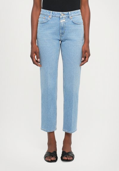 Lys blå denim jeans med høj talje, lige ben og rå kant. Forlomme med orange syning. Bæres med sorte flade sandaler.