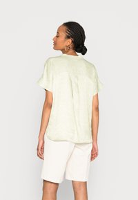 Top verde claro de manga curta com padrão geométrico, corte descontraído, bainha arredondada e textura suave, combinado com calções brancos.