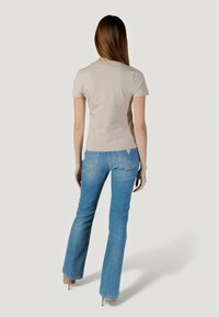 Top beige de manga corta con un diseño ajustado, combinado con jeans acampanados azul claro que cuentan con una pequeña etiqueta con logo en el bolsillo trasero.