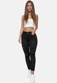 Skinny black jeans with ripped details, high waist design, and cuffed hems, paired with a white cropped top and white sneakers.