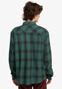 Grønternet flannel skjorte med sort ternet mønster, knapmanchetter, almindelig krave og buet kant. Blødt, tekstureret stof.