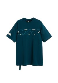 Camiseta de algodón de gran tamaño en color azul verdoso, con un logo "MWM" bordado texturizado, acentos plateados y un detalle de pestaña lateral en un diseño minimalista.