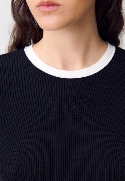 Camisa de punto negra con cuello blanco. Presenta un logo texturizado en el centro, textura suave y diseño ajustado.