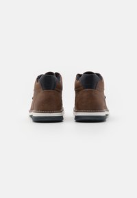 Brune lædersneakers med en tekstureret overdel, kontrasterende marinblå accenter, hvid mellemsål og sort gummisål. Synlig stikning.