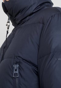 Chaqueta acolchada azul marino con alto cuello, cierre frontal y bolsillo lateral. Textura suave con un diseño ligero.