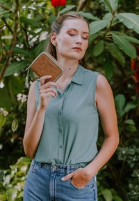 Cork wallet with a tan and blue design held by a person wearing a light green sleeveless shirt and blue jeans against a green background.