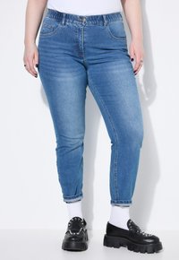 Světle modré džíny s tapered nohavicemi, elastickým pasem a tradičním pěti kapsovým designem. V kombinaci s černými platformovými botami a bílými ponožkami.