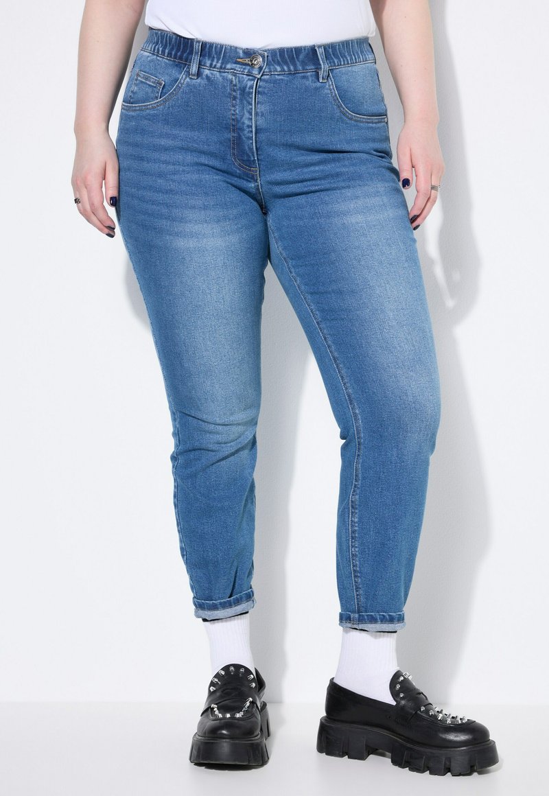 Světle modré džíny s tapered nohavicemi, elastickým pasem a tradičním pěti kapsovým designem. V kombinaci s černými platformovými botami a bílými ponožkami.