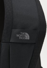 Detailný záber na čierny látkový batoh s textúrovaným povrchom a šedou označovacou nálepkou "The North Face."