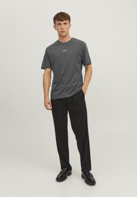 Szary T-shirt z krótkim rękawem z bawełny, z okrągłym dekoltem i małym logo na piersi, w zestawie z czarnymi luźnymi spodniami i czarnymi butami.