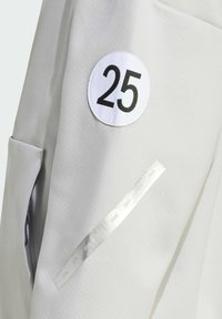 Grauer Stoff mit glatter Textur zeigt einen großen runden weißen Fleck mit der Zahl "25" und einem silbernen Streifen mit eingravierten Jahren, 2018-2021.