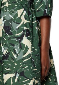 Robe verte avec un motif de feuilles en noir et crème, fabriquée en tissu léger, avec des manches courtes et une coupe décontractée.