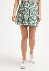 Vit kjol med ett grönt blommönster och paisleymönster, med elastisk midja och utsvängd silhuett. Bärs med vita sneakers.