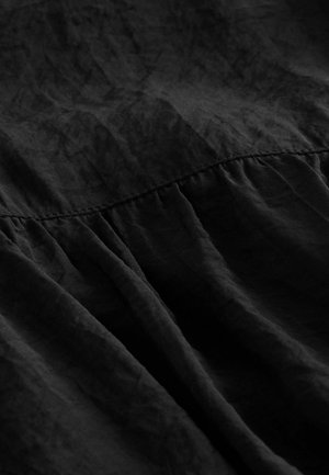 Tissu noir avec une texture froissée, comportant des détails froncés le long de la couture. Matériau doux et léger avec une finition mate.