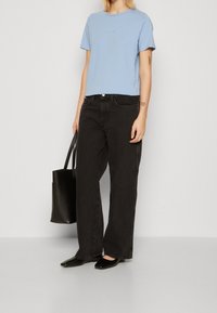 Ljusblå t-shirt med kort ärm, svarta vida jeans, svarta flator och en svart tote-väska, klädd med en enkel design och utan anmärkningsvärda mönster.