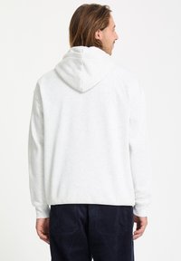 Haut à capuche gris clair avec une capuche spacieuse, des manches longues et un tissu texturé. Il présente une coupe décontractée et des poignets en côte au niveau des poignets et de l'ourlet.