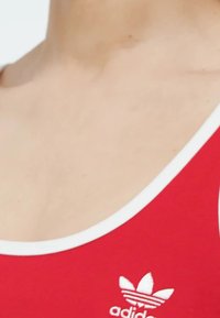 Punainen hihaton urheilupaita, jossa on valkoinen reunus. Etupuolella pieni valkoinen Adidas-logo. Kangas näyttää sileältä.