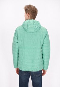 Muntgroene, puffy jacket met een capuchon, met gestikte horizontale lijnen en een gladde, glanzende textuur; gedragen over donkere jeans.