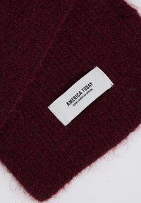 Burgundy wool blend fabric with a textured finish, featuring a white label reading "AMERICA TODAY" and "ICONIC AMERICAN APPAREL."