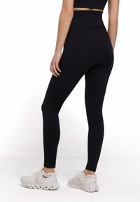 Black high-waisted leggings with textured pattern, form-fitting design, and smooth fabric. Worn with white athletic shoes.
