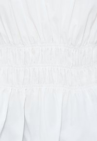 Tissu blanc avec plusieurs rangées horizontales de smocks élastiques froncés créant un motif texturé et plissé.