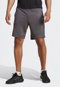 Graue Sportshorts mit elastischem Bund, seitlichen Taschen und schwarzen Akzenten. Kombiniert mit schwarzen Turnschuhen und einem schwarzen T-Shirt.