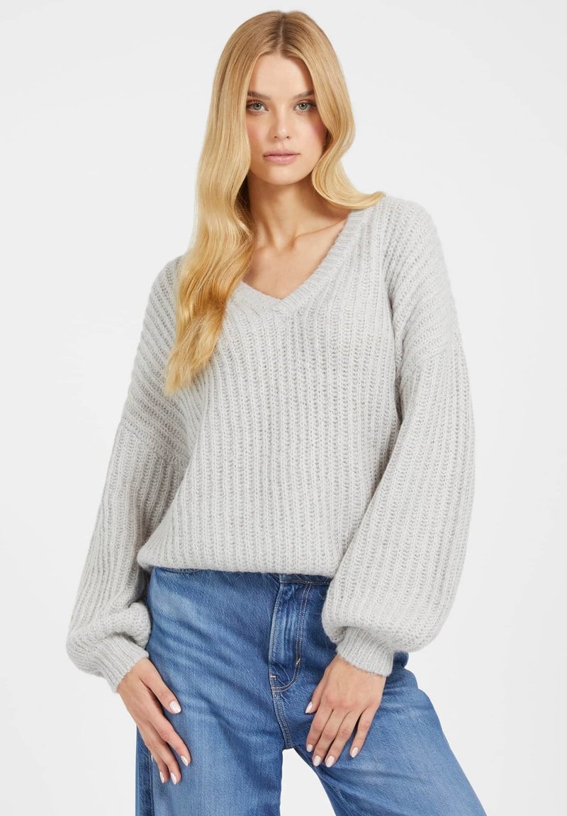 Hellgrau gestrickter Pullover mit V-Ausschnitt, geripptem Muster und lockeren, voluminösen Ärmeln. Kombiniert mit blauen Denim-Jeans.