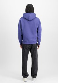 Lila huvtröja med avslappnad passform, ribbade ärmslut och nederkant. Matchad med mörkgrå jeans i avslappnad passform och ljusa sneakers.