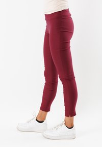 Leggings color bordeaux con un design aderente, realizzati in materiale elasticizzato, con spaccature laterali all'orlo, abbinati a sneakers bianche.