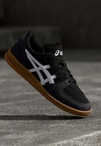 Black and gray sneaker with white side stripes, suede and mesh materials, rubber sole, and breathable design. Features perforated toe area.