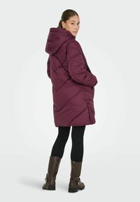 Lilla pufferjakke med hætte, der har chevron-syningsdetaljer. Båret over sorte leggings og brune knæstøvler.