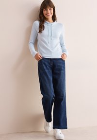 Ljusblå rippad långärmad tröja med huva och dragsko, matchad med lösa mörkblå denimbyxor och vita sneakers.