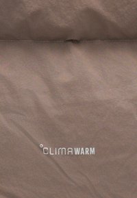 Pruun kangas sileda tekstuuriga, millel on valge tekst "CLIMAWARM", paigutatud madalamale sektsiooni.