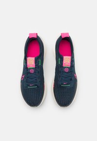 Ett par marinblå atletiska sneakers med rosa innersulor och detaljer, vita sulor och QR-koder på starkt rosa tungaetiketter, sedda uppifrån.