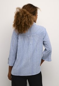 Camicia a maniche lunghe a righe verticali blu e bianche, con una piega sul retro e maniche arrotolabili. Realizzata in tessuto leggero e testurizzato.