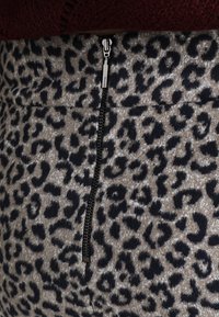 Falda de estampado de leopardo con base beige y manchas negras. Presenta una cremallera negra vertical en el centro frente, con una textura suave.