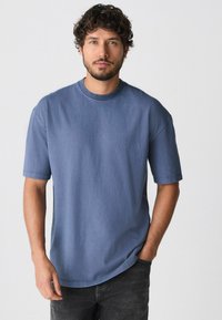 Kurzärmliges Rundhals-T-Shirt aus weichem, mittelblauem Stoff; lockere Passform mit glatter Textur und dezenten Stichdetails.