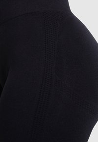 Gros plan sur des leggings noirs sans couture montrant des motifs de points texturés le long du côté et de la ceinture sur un fond clair.