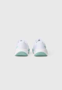 Zapatos deportivos blancos con suelas verde claro, vistos desde la parte trasera, sobre un fondo blanco liso.