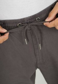 Graue Hose mit elastischem Bund und geflochtenem Kordelzug, ausgestattet mit Edelstahlspitzen, glatter Textur und lockerer Passform.