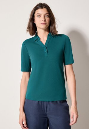 Teal lyhythihainen polo-paita, jossa on kaulus ja kolmen napin napitus, yhdistettynä tummiin housuihin; sileä kankaan rakenne.