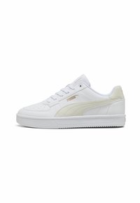 Baskets Puma basses blanches avec rayure beige sur le côté, bout perforé, fermeture à lacets et semelle en caoutchouc plate, présentées de profil.