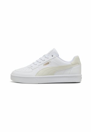 Vit låg sneaker från Puma med beige sidostrack, perforerad tå, snörning och platt gummisula, visad i profil.