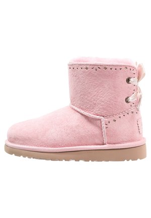 Różowy zamszowy botek za kostkę z futrzanym wyściółką, ozdobnymi wycięciami u góry oraz sznurowaniem z satynowej wstążki z tyłu, płaska beżowa podeszwa.