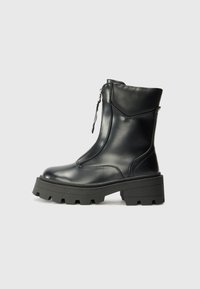 Botte cheville en cuir noir avec une semelle en caoutchouc épaisse, fermeture éclair latérale, texture lisse et design minimaliste, présentant des détails de couture subtils.