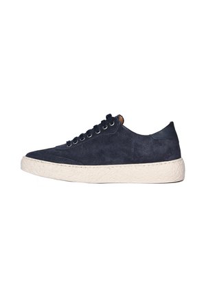 Sneaker scamosciata blu scuro a taglio basso con lacci neri e suola spessa in gomma bianco sporco con texture, vista di lato su sfondo bianco.