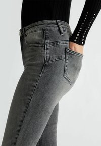 Jeans de mezclilla grises con una cintura alta, corte ajustado y un diseño clásico de bolsillos traseros. El material tiene una textura suave con un ligero efecto desgastado.