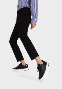 Sneakers platform in pelle nera con suole bianche, caratterizzati da un design testurizzato e lacci neri, abbinati a jeans neri cropped e una maglietta a righe.