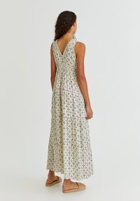 Vestido maxi en crema con patrones dispersos en azul oscuro, diseño de espalda en V, volantes en capas y tela suave. Llevado con sandalias planas de color marrón claro.
