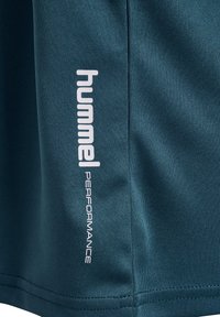 Teal sportshorts i texturerad tyg med en vit "hummel"-logotyp och "PERFORMANCE"-text längs sidan.